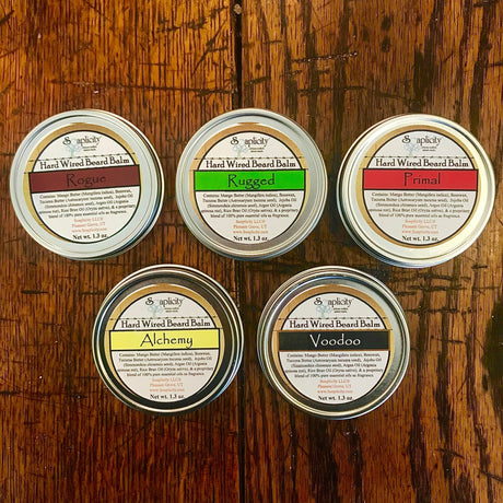 Alchemy Hard Wired Beard Balm tin among other scented beard balms on wooden surface